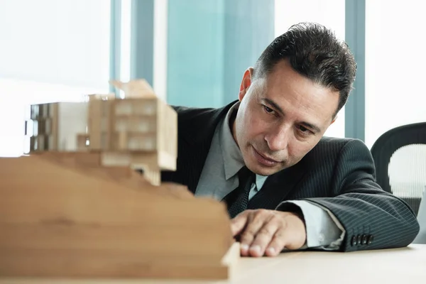 Selbstbewusster Geschäftsmann blickt auf Architektur-Miniaturhaus-Projekt — Stockfoto