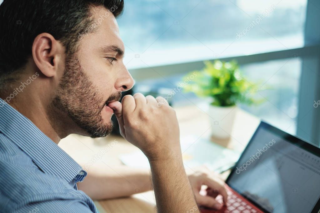 Anxious Businessman Biting Nails Working With Laptop Computer In Office