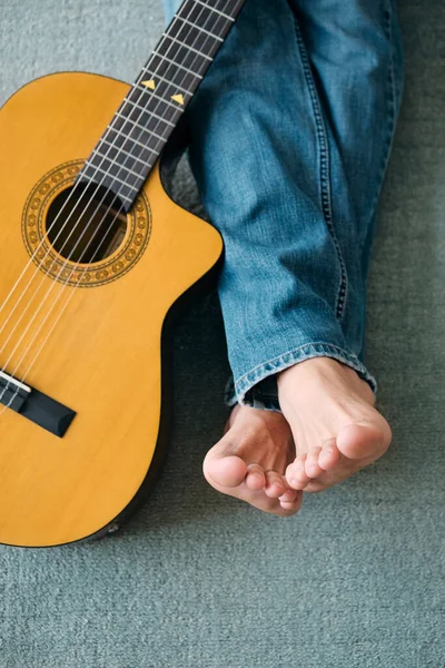 Guitarrista descalço com pernas estendidas ao lado da guitarra — Fotografia de Stock