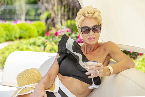 Güzel olgun sarışın bikini modeli, açık havada bir yüzme havuzu pozlar.