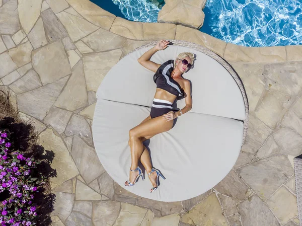 Güzel olgun sarışın bikini modeli, açık havada bir yüzme havuzu pozlar.