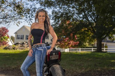 Güneşli bir günde güzel bir sarışın manken motosikletle poz veriyor.