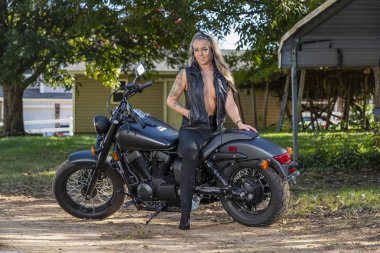 Güneşli bir günde güzel bir sarışın manken motosikletle poz veriyor.