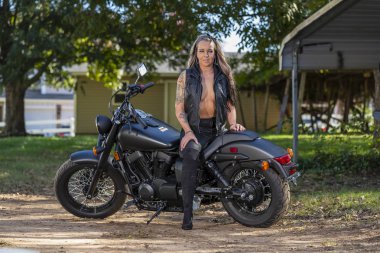 Güneşli bir günde güzel bir sarışın manken motosikletle poz veriyor.