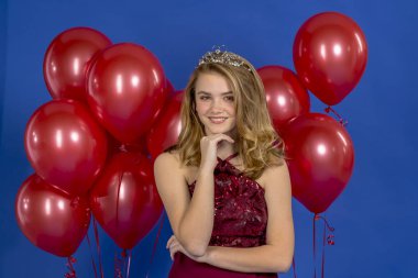 Bir stüdyo ortamında kamera önünde bir taç ve kırmızı balonlar poz güzel bir sarışın genç model