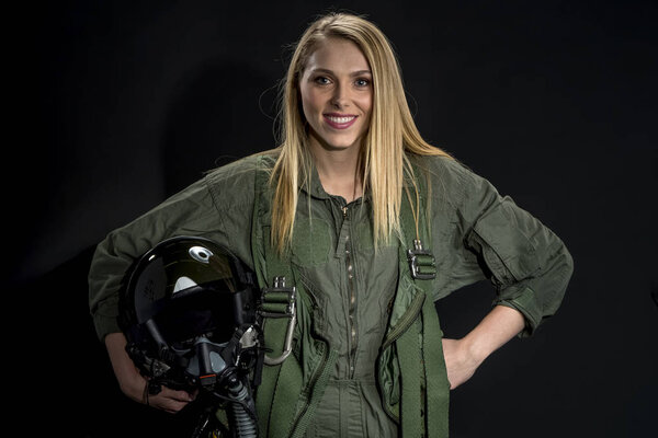 A female fighter pilot poses against a black background in a studio environment 