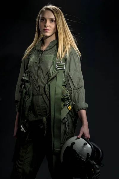 A female fighter pilot poses against a black background in a studio environment