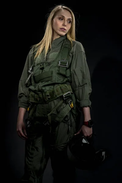 A female fighter pilot poses against a black background in a studio environment