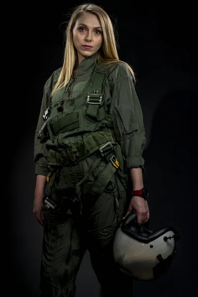 A female fighter pilot poses against a black background in a studio environment