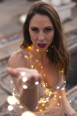 Muhteşem bir İspanyol esmer model gün batımında küçük ışıklarla dışarıda poz veriyor.