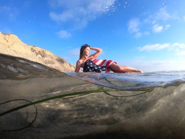 Una encantadora modelo morena posa desnuda en la costa con un americano —  Fotos de Stock