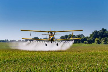 A crop duster applies chemicals to a field of vegetation. clipart