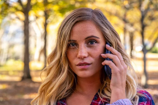 A gorgeous blonde model talks on her cellphone on an autumn day outdoors in a park