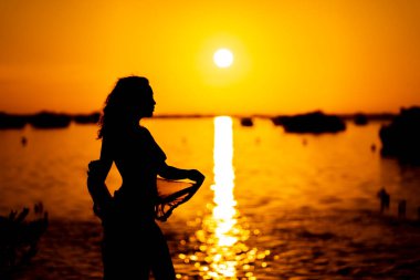 Güzel, çıplak bir Latin model, egzotik bir Karayip plajında güneşin doğuşuyla poz verirken siluete bürünür.