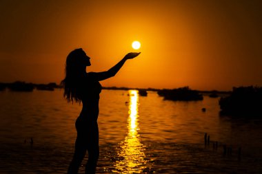 Güzel, çıplak bir Latin model, egzotik bir Karayip plajında güneşin doğuşuyla poz verirken siluete bürünür.