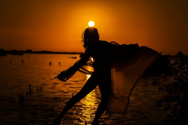 A beautiful latin model is silhouetted as she poses with the rising sun behind her on a exotic Caribbean beach