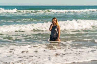 Sarışın bir kadın kumsalda tek başına eğleniyor.