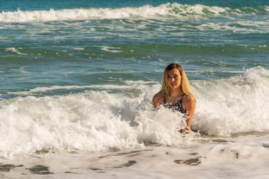 Sarışın bir kadın kumsalda tek başına eğleniyor.