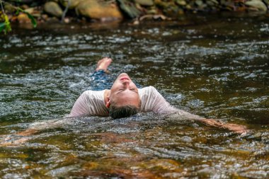 Muhteşem bir sarışın manken bir yaz günü ormanda bir nehirde oyun oynuyor.
