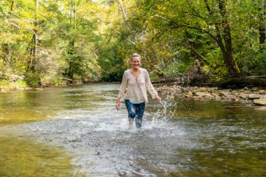 Muhteşem bir sarışın manken bir yaz günü ormanda bir nehirde oyun oynuyor.