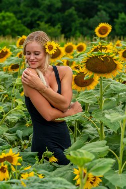 Sarışın bir model, yaz gününün tadını çıkarırken ayçiçeği tarlasında poz veriyor.