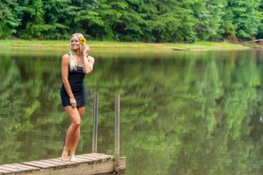 Muhteşem sarışın bir manken, yaz gününün tadını çıkarırken göletin kenarında poz veriyor.