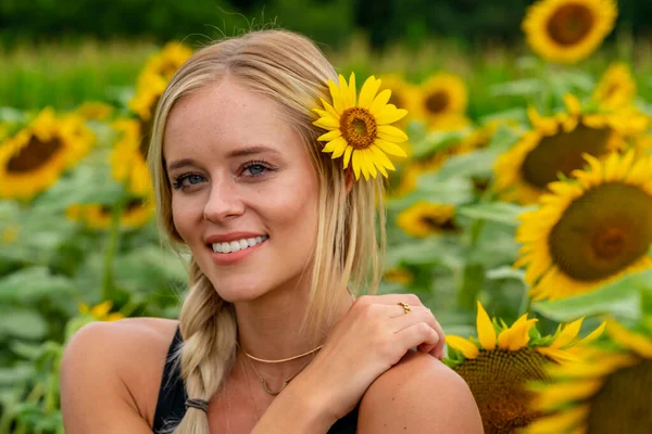 Sarışın bir model, yaz gününün tadını çıkarırken ayçiçeği tarlasında poz veriyor.