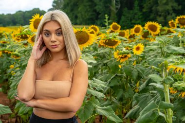 Sarışın bir model, yaz gününün tadını çıkarırken ayçiçeği tarlasında poz veriyor.