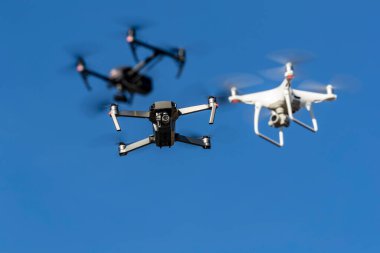 Bir grup dron havada mavi gökyüzüne karşı uçuyor.