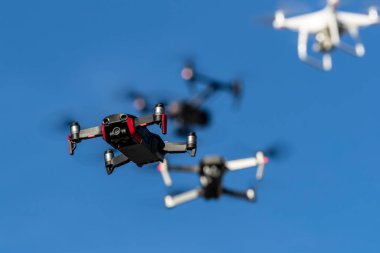 Bir grup dron havada mavi gökyüzüne karşı uçuyor.