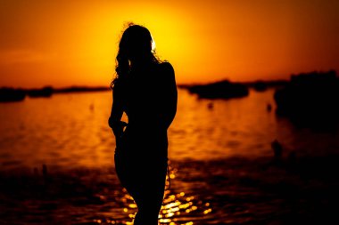 Güzel bir latin modeli, egzotik bir Karayip plajında güneşin doğuşuyla poz verirken siluetlenir.