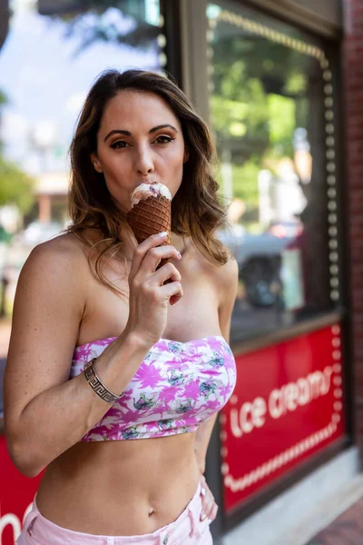 都会の中でアイスクリームを食べながら屋外でポーズをとる美しいブルネットモデル — ストック写真
