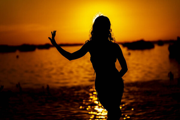 A beautiful latin model is silhouetted as she poses with the rising sun behind her on a exotic Caribbean beach