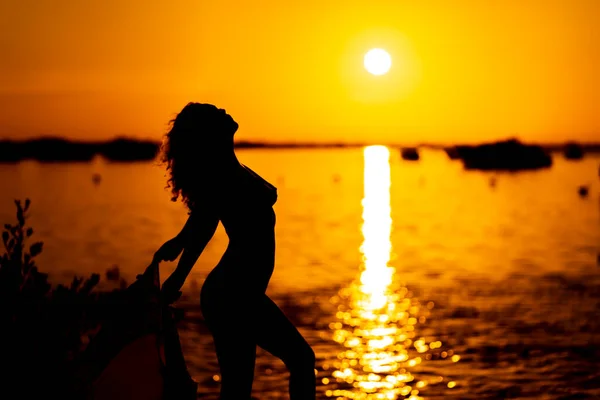 美しいラテン語のヌードモデルがシルエットになっています 彼女はエキゾチックなカリブ海のビーチで彼女の後ろに昇る太陽と一緒にポーズをとっています — ストック写真