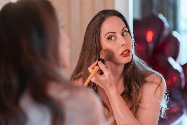 A beautiful Portuguese model puts on makeup in a mirror before a party