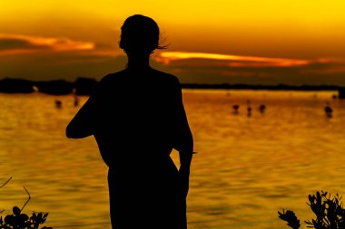 Güzel bir latin modeli, egzotik bir Karayip plajında güneşin doğuşuyla poz verirken siluetlenir.