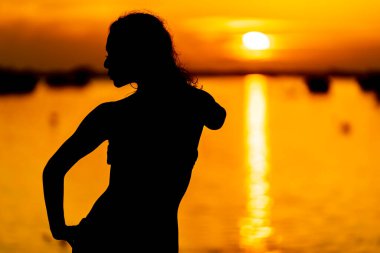 Güzel bir latin modeli, egzotik bir Karayip plajında güneşin doğuşuyla poz verirken siluetlenir.