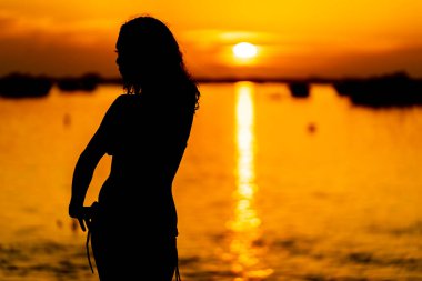 Güzel bir latin modeli, egzotik bir Karayip plajında güneşin doğuşuyla poz verirken siluetlenir.