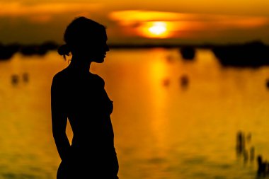 Güzel, çıplak bir Latin model, egzotik bir Karayip plajında güneşin doğuşuyla poz verirken siluete bürünür.