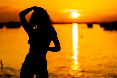 Güzel bir latin modeli, egzotik bir Karayip plajında güneşin doğuşuyla poz verirken siluetlenir.