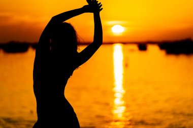 Güzel bir latin modeli, egzotik bir Karayip plajında güneşin doğuşuyla poz verirken siluetlenir.