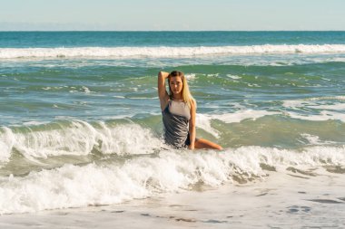 Sarışın bir kadın kumsalda tek başına eğleniyor.