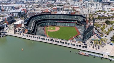 An aerial view of McCovey Cove shows boats and kayaks gathering beneath Oracle Parks right field, where fans await home run balls in the scenic waters of San Francisco Bay.