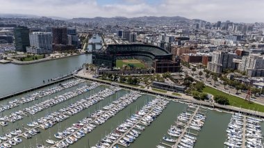 An aerial view of McCovey Cove shows boats and kayaks gathering beneath Oracle Parks right field, where fans await home run balls in the scenic waters of San Francisco Bay.