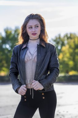 A beautiful young brunette poses gracefully for the camera, her smile glowing as she enjoys the crisp fall air, surrounded by golden leaves on a perfect autumn day.