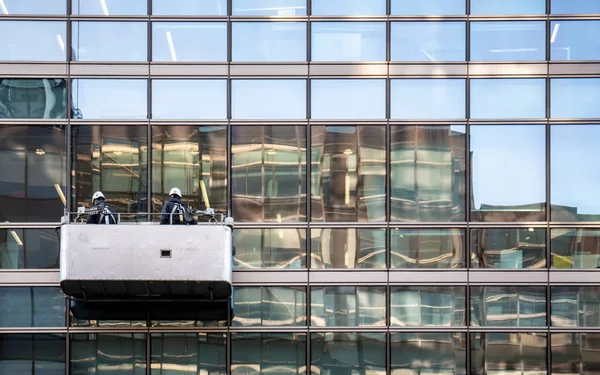 Windows cleaners making use of a cradle to clean the exterior of a contemporary office block.