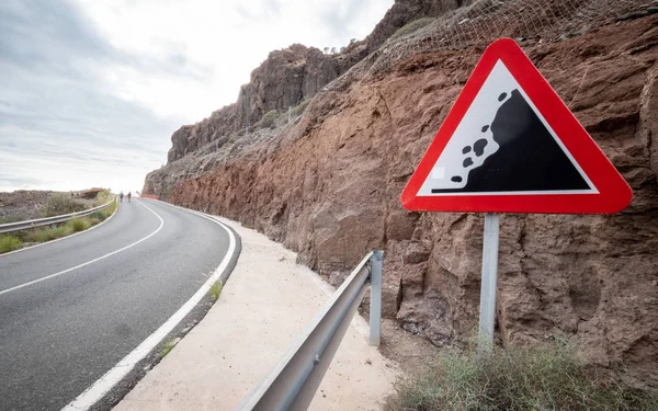 Road Warning sign: Falling Rocks. A triangular street sign giving warning of potential falling rocks and debris in the road.