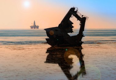 Bir petrol platformunun arka planda geminin enkazı