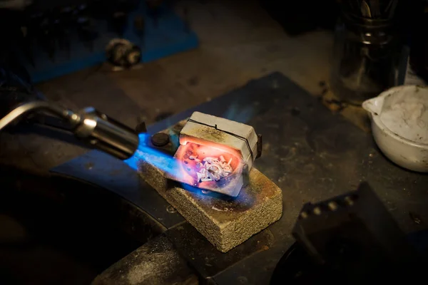 Jeweler melts with a flame silver or gold on old workbench in jewelers workshop