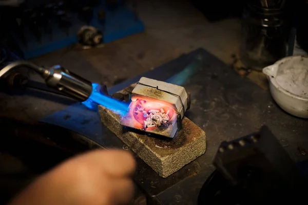 Jeweler melts with a flame silver or gold on old workbench in jewelers workshop